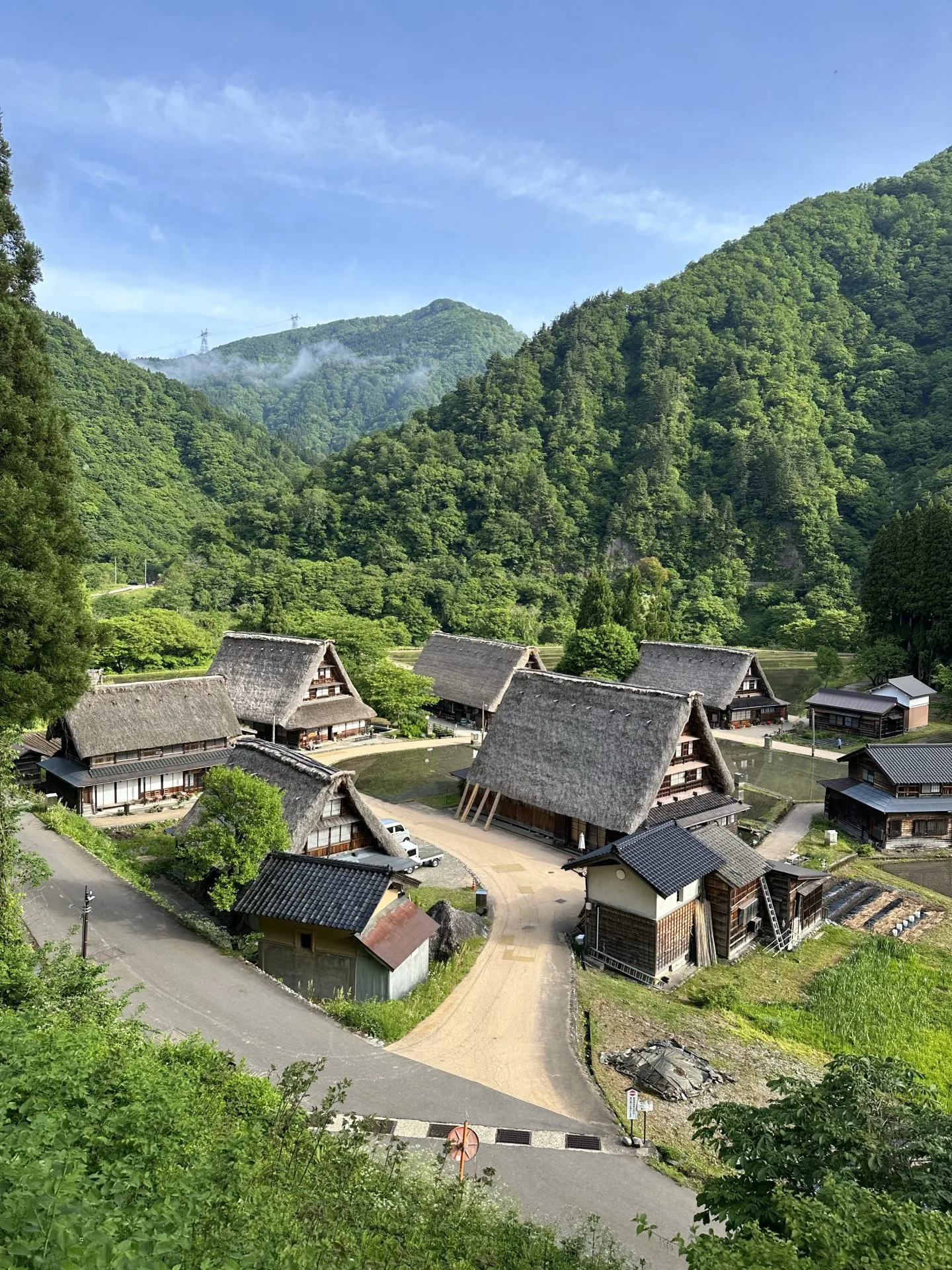 緑の山々に囲まれた合掌造り集落を上から望む