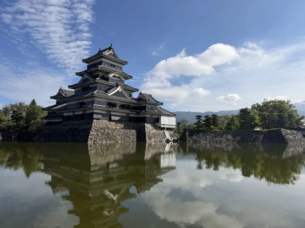 朝の松本城。青空の下、黒い天守がお堀の水面に映っている